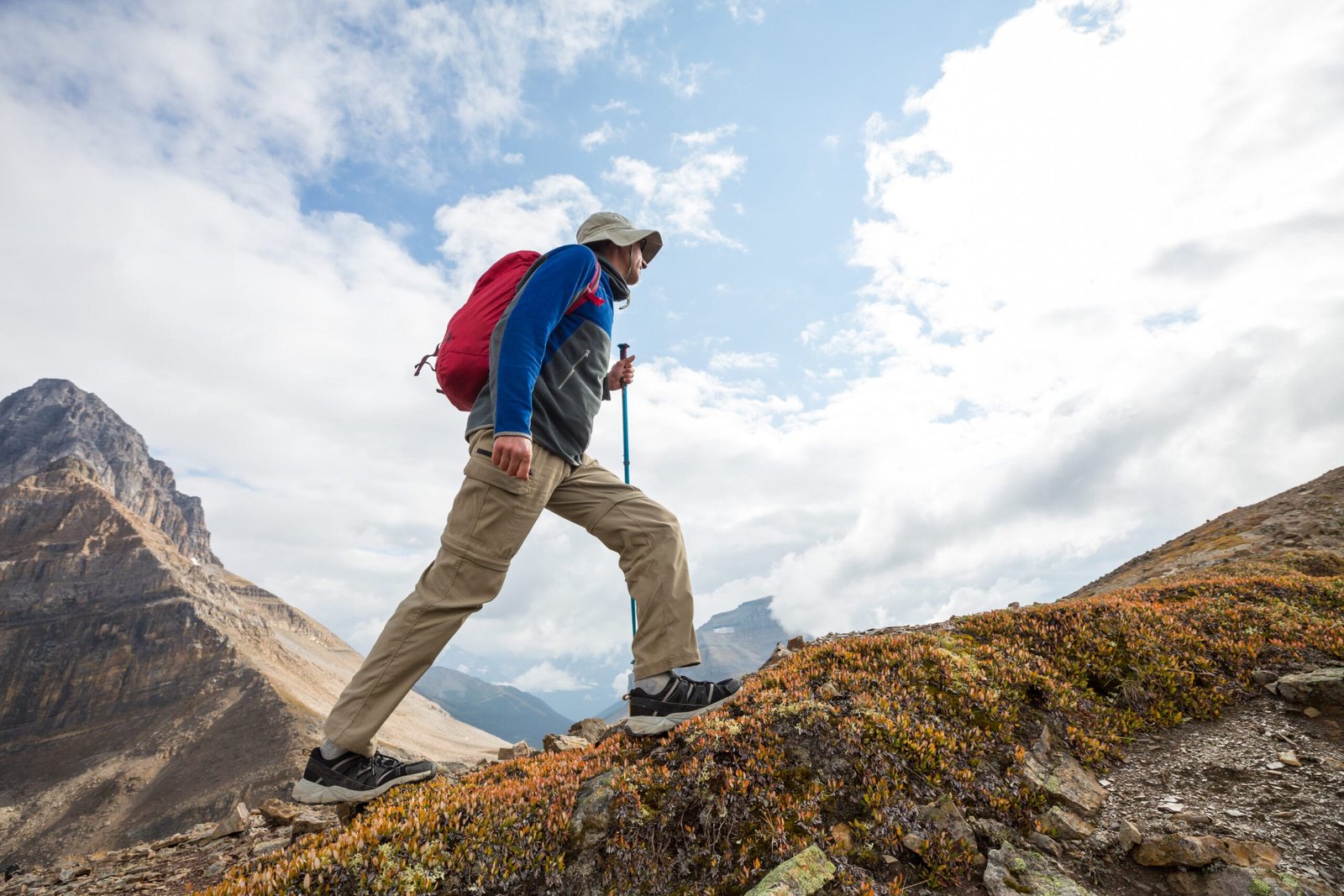 Man hiking up rocky mountain trail with trekking pole, showing the physical toll on feet during climbs, ideal context for custom insoles for mountain climbing.