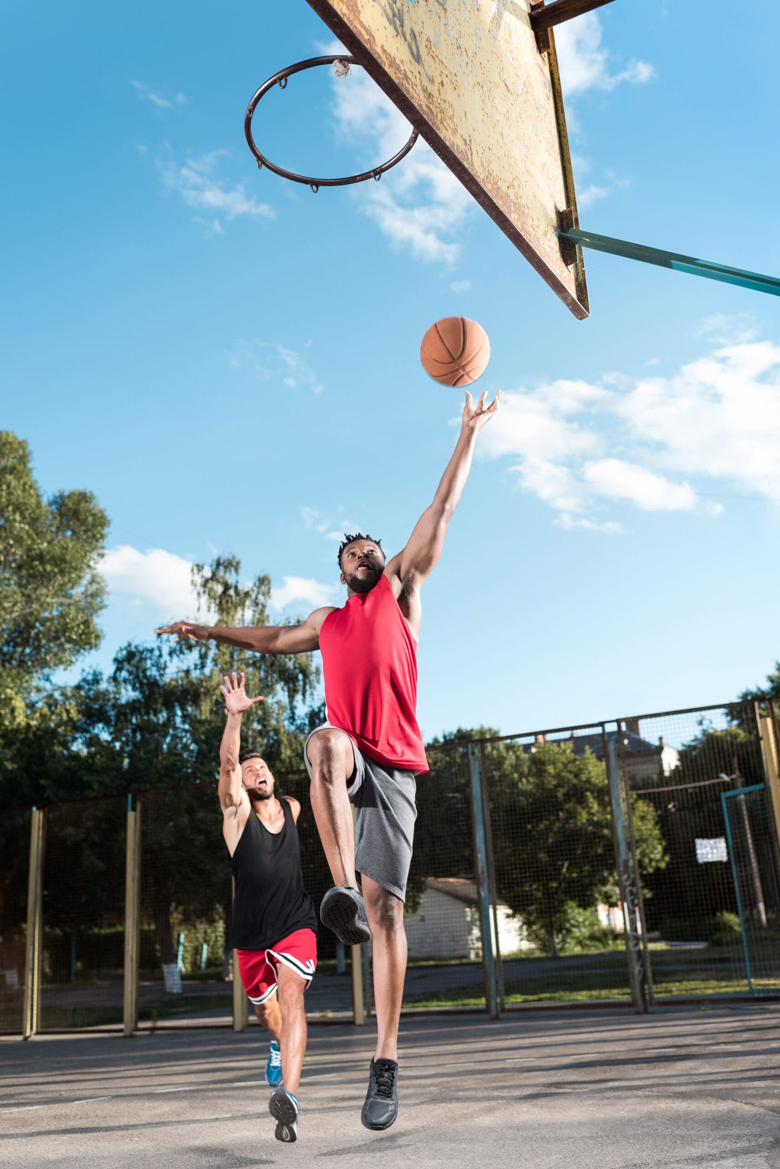 Two basketball players in action on an outdoor court, with the player in red performing a layup—showcasing how basketball insoles can enhance game performance.