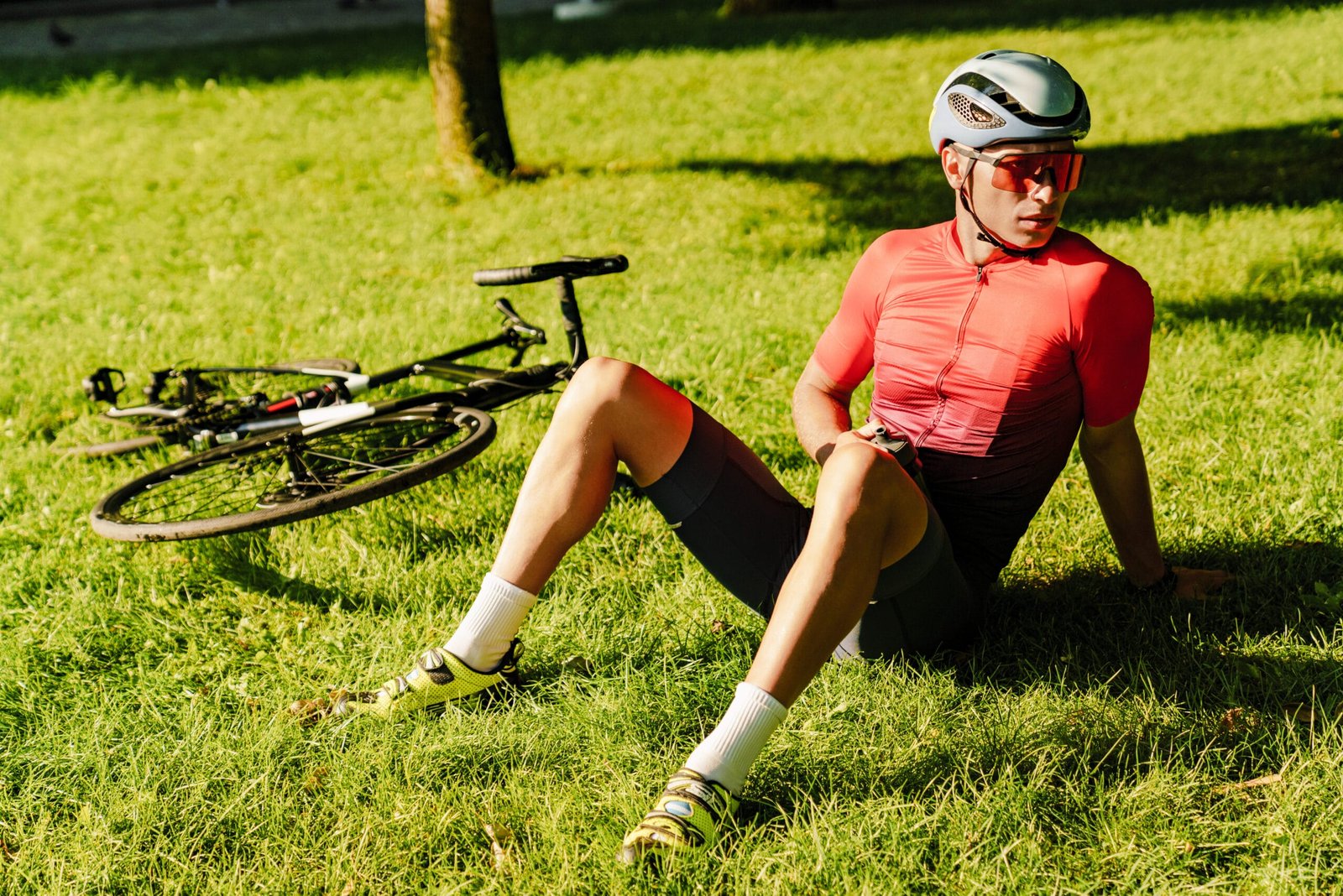 Cyclist resting on grass after a ride, wearing helmet and cycling shoes, emphasizing the need for insoles to prevent cycling foot numbness.